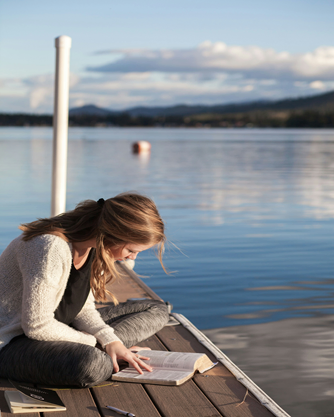 a lady reading the bible while sitting on the boardwalk by the lake